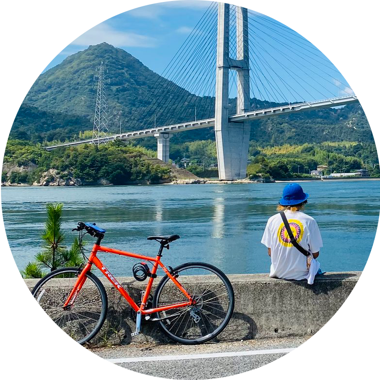 しまなみ海道の道沿いで自転車を停めて橋と海を眺めて休憩している写真